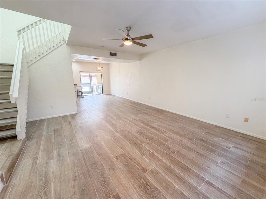 An open living area features wood-look tile flooring, a ceiling fan, and a staircase — 3460 COUNTRYSIDE #60 BOULEVARD, CLEARWATER, FL