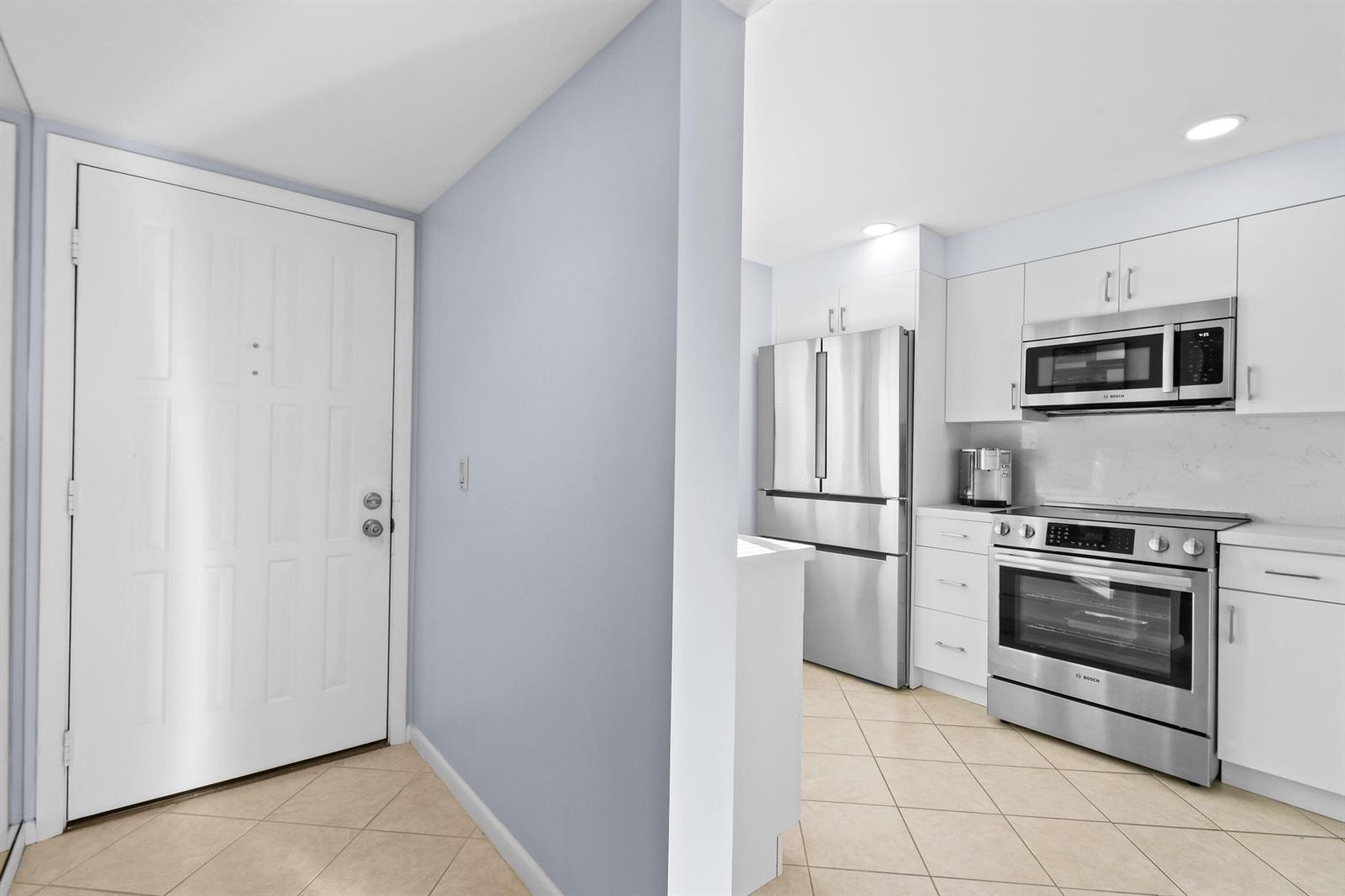 A white door opens into a kitchen with stainless steel appliances and light tile flooring — 501 S Seas Drive # 206, Jupiter FL 33477, JUPITER, FL