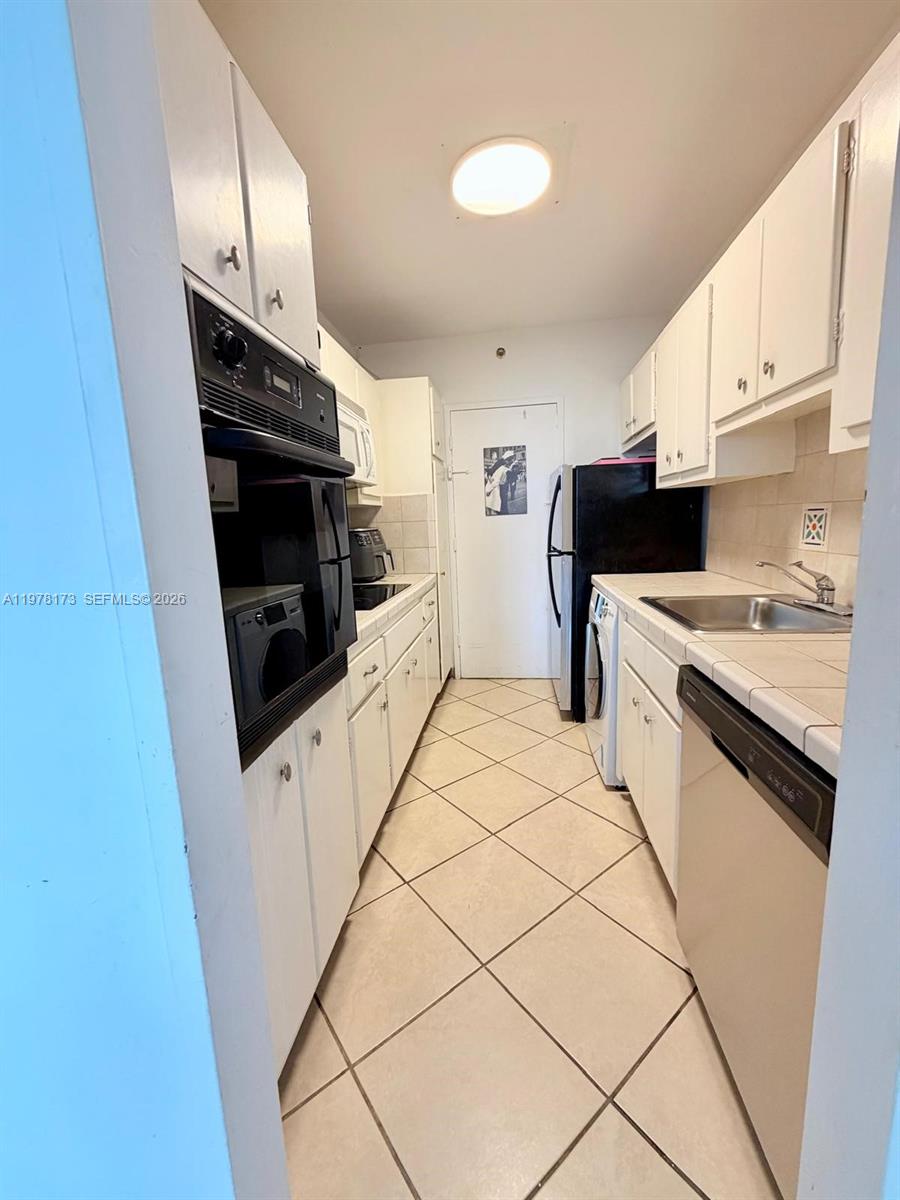This galley-style kitchen features white cabinets, a double wall oven, and tiled flooring — 100 Lincoln Rd # 441, Miami Beach FL 33139, MIAMI BEACH, FL