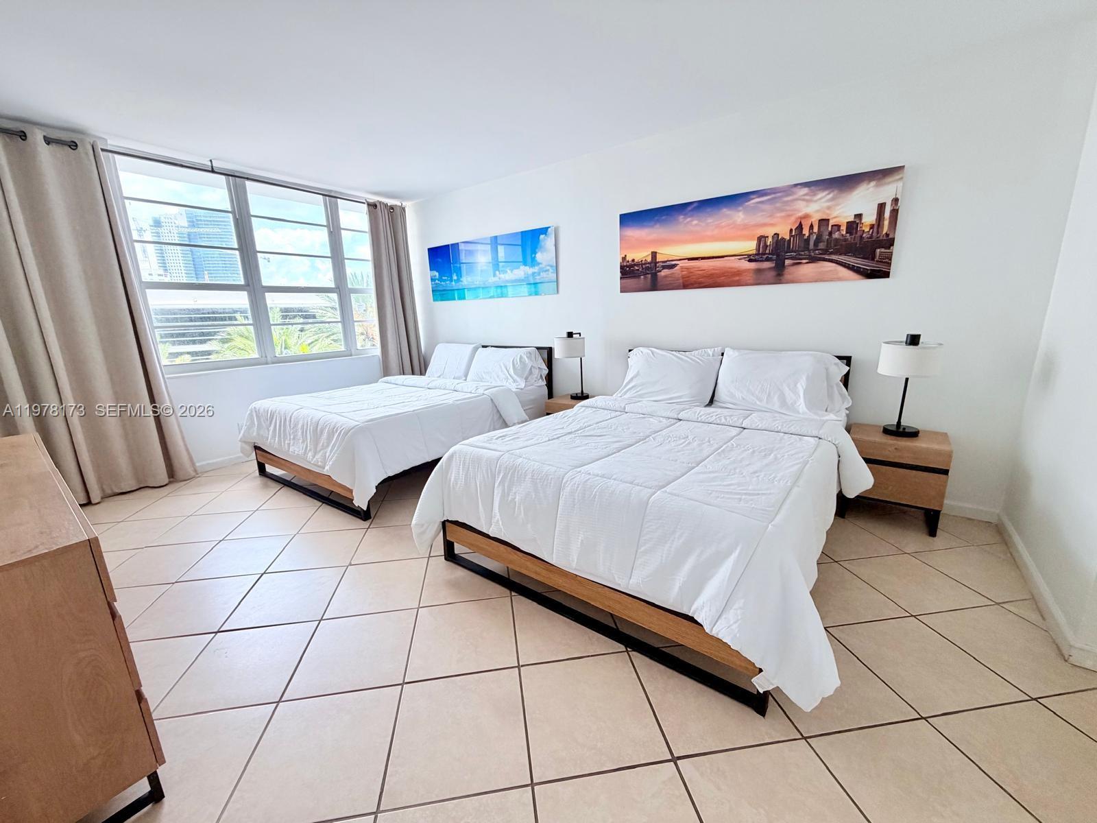 A bedroom features two beds with white bedding, tile floors, and large windows with curtains — 100 Lincoln Rd # 441, Miami Beach FL 33139, MIAMI BEACH, FL