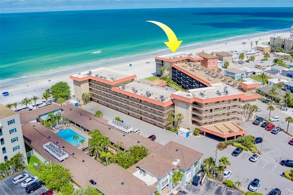 An aerial view shows a multi-story beachfront hotel complex with a swimming pool and parking — 17580 GULF BOULEVARD UNIT 412, REDINGTON SHORES, FL