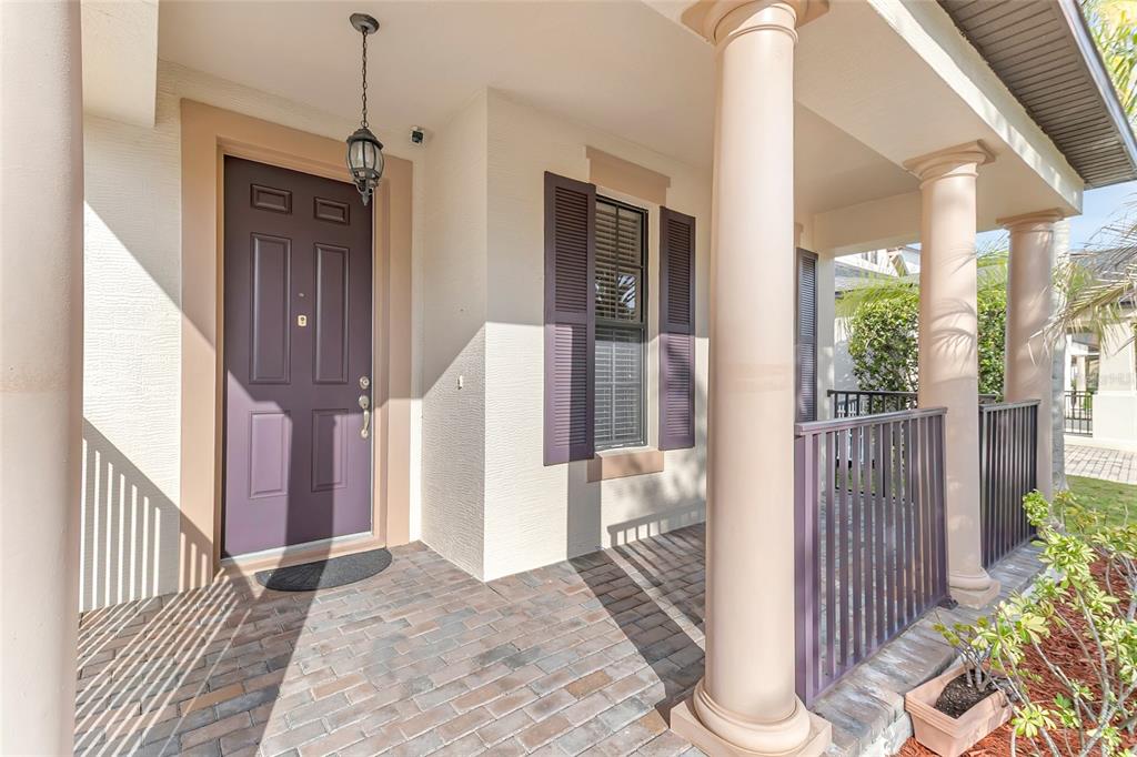A covered front porch features a purple door, brick flooring, and white columns — 9837 OLD PATINA WAY, ORLANDO, FL
