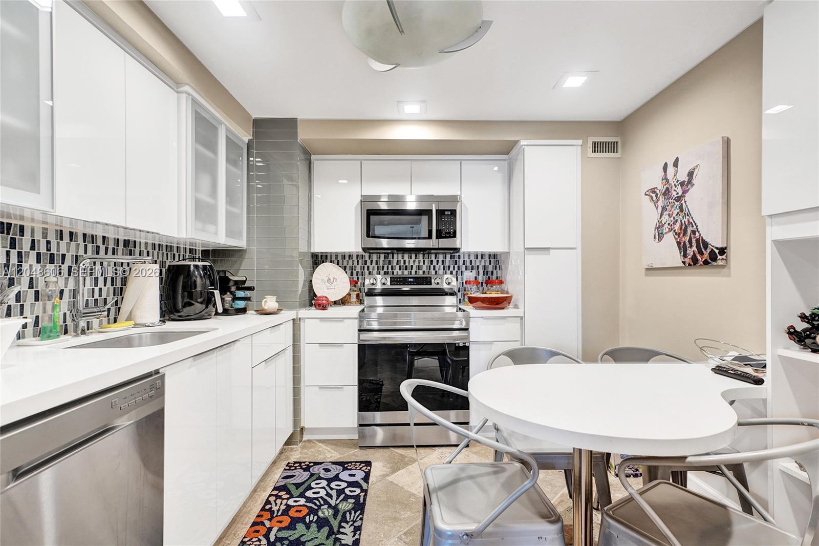 A modern kitchen features white cabinetry, stainless steel appliances, and a small dining table — 9225 Collins Ave # 1402, Surfside FL 33154, SURFSIDE, FL
