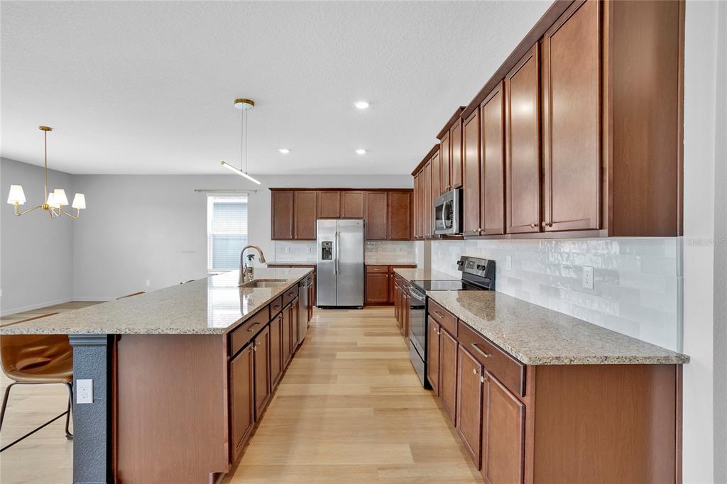 A kitchen features dark wood cabinets, granite countertops, stainless steel appliances, and light wood flooring — 777 OGELTHORPE DRIVE, DAVENPORT, FL