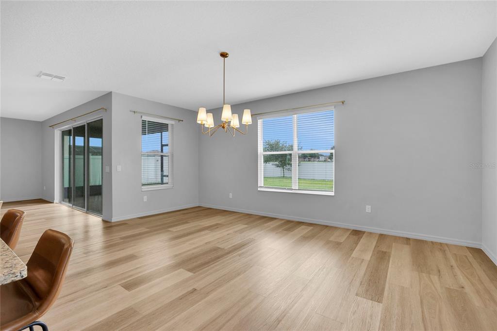 A dining area with light wood floors, a chandelier, and windows overlooking a backyard — 777 OGELTHORPE DRIVE, DAVENPORT, FL