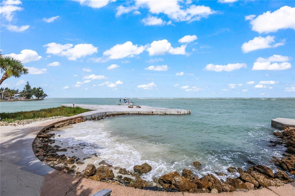 A concrete pier extends into a bay with rocky shoreline and a small boat nearby — 220 PASS KEY ROAD UNIT 220, SARASOTA, FL