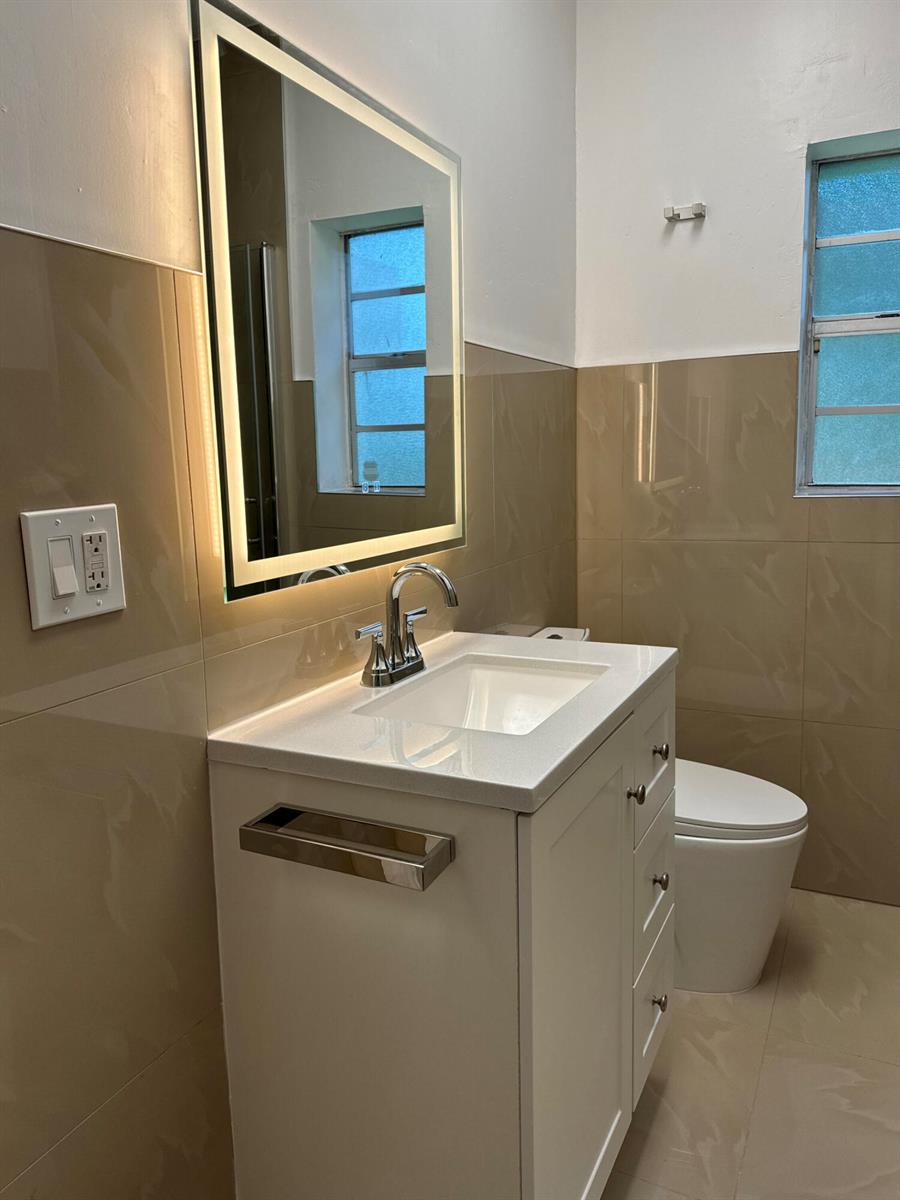 A bathroom featuring a white vanity, a lighted mirror, and beige tiled walls — 701 SW 8th Avenue, Delray Beach FL 33444, DELRAY BEACH, FL