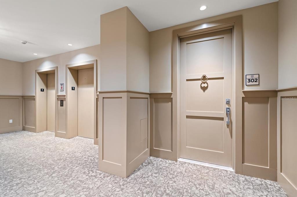 A hallway features two elevators and a door labeled 302 with beige wainscoting and carpeting — 125 BELLEVIEW BOULEVARD UNIT 302, BELLEAIR, FL