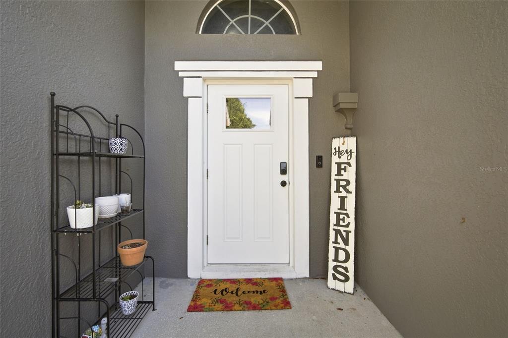 A white front door with a transom window sits beside a metal shelving unit — 19517 ARDWICK WAY, LAND O LAKES, FL