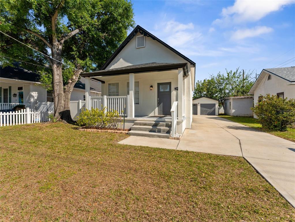 A white house with a front porch, concrete driveway, and detached garage sits on a lawn — 2903 W IVY STREET, TAMPA, FL