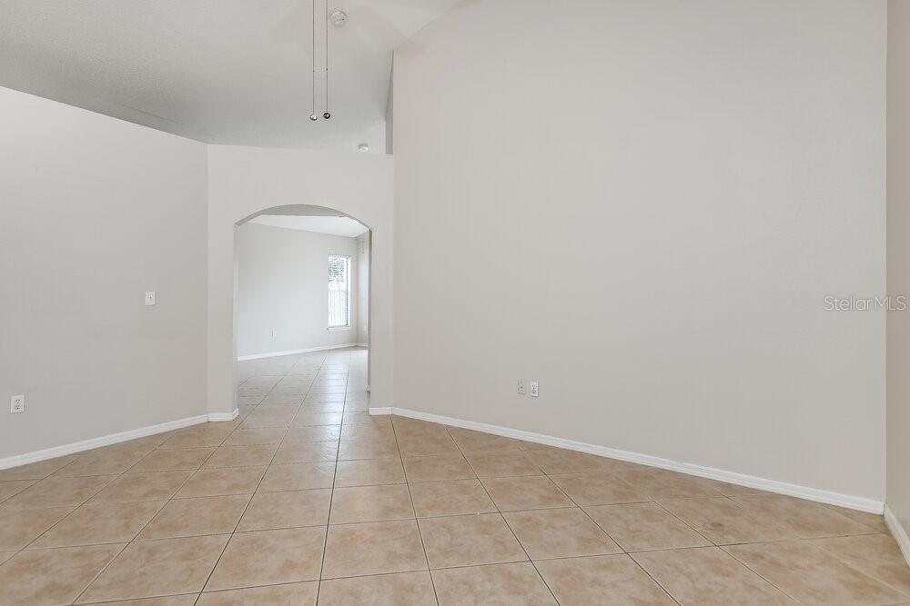 An empty room with beige tile flooring and an arched doorway leading to another space — 10832 RUSHWOOD WAY, CLERMONT, FL