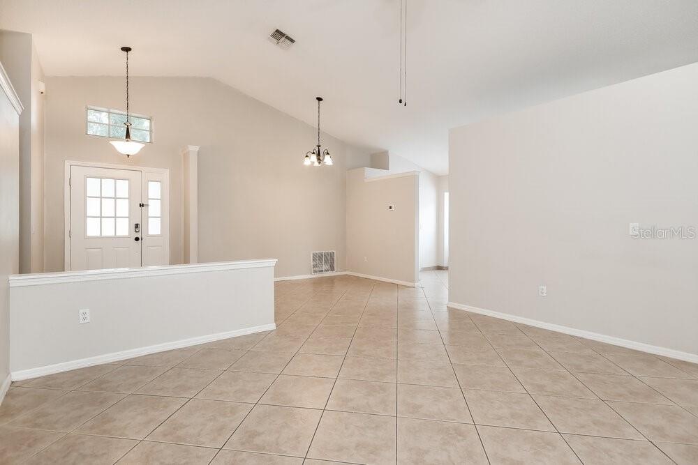 An empty room with beige tile flooring, vaulted ceilings, and a white front door — 10832 RUSHWOOD WAY, CLERMONT, FL