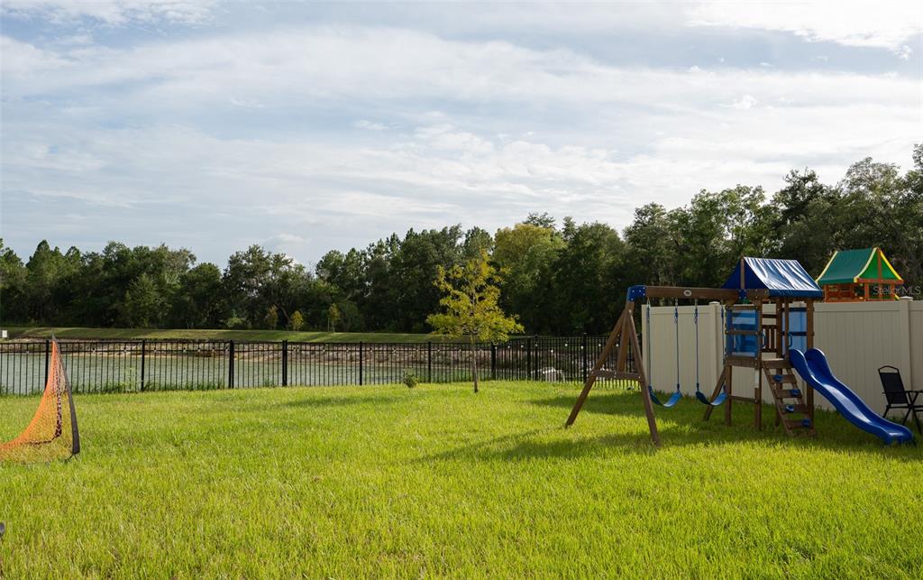 The rear exterior of a two-story tan house features a backyard with a swing set — 35606 KINSEY POINT, ZEPHYRHILLS, FL
