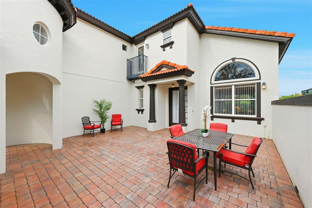 A paved patio features a dining set with red chairs and a small balcony above — 910 LASCALA DRIVE, WINDERMERE, FL
