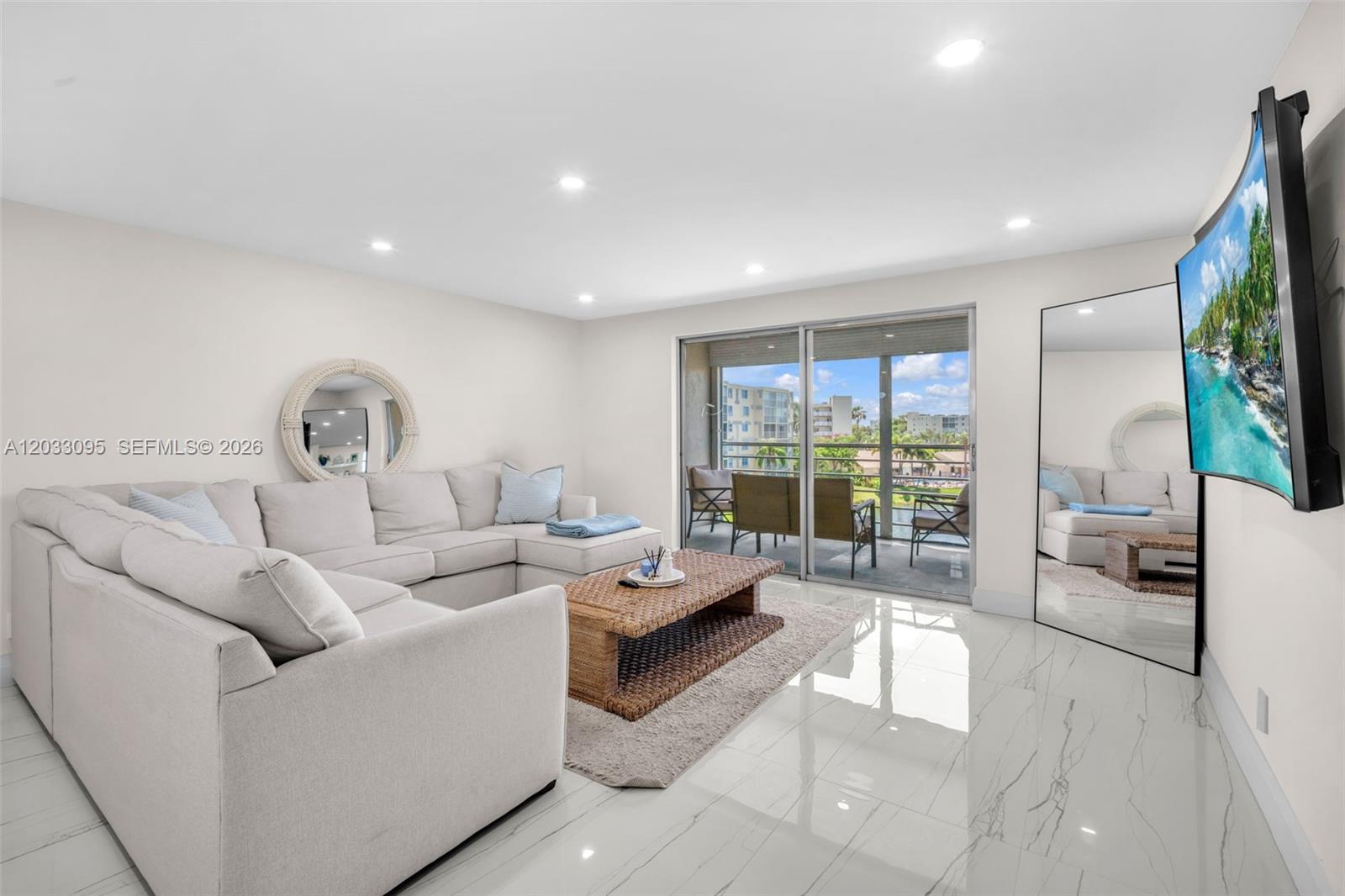 A living room features a sectional sofa, a wicker coffee table, and a large mirror — 441 SE 3rd St # 404, Dania Beach FL 33004, DANIA BEACH, FL