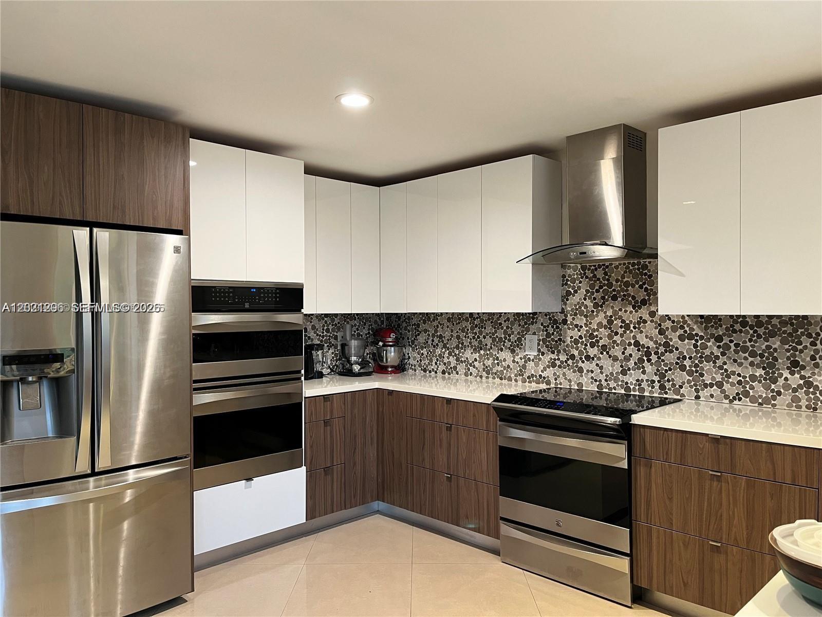 A modern kitchen features two-tone wood and white cabinetry with stainless steel appliances — 2001 NE 214th St, Miami FL 33179, MIAMI, FL