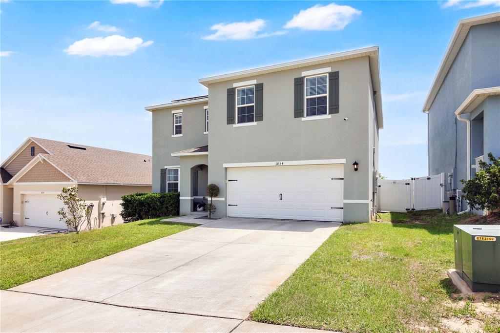 A two-story house with a light gray exterior, a two-car garage, and a concrete driveway — 1854 JUNEBERRY STREET, CLERMONT, FL