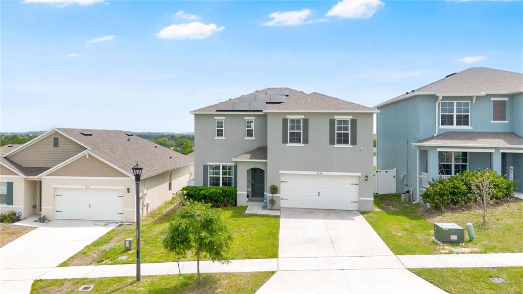 A two-story suburban house with a gray exterior, a two-car garage, and rooftop solar panels — 1854 JUNEBERRY STREET, CLERMONT, FL