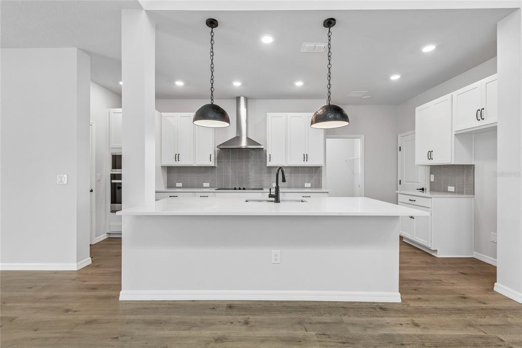 A modern kitchen features white upper cabinets, a dark island with a dishwasher, and pendant lighting — 626 KINGSWOOD COURT, BRADENTON, FL