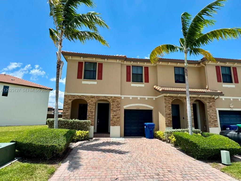 A two-story townhouse features a stone facade, red shutters, and a brick paver driveway — HOMESTEAD, FL