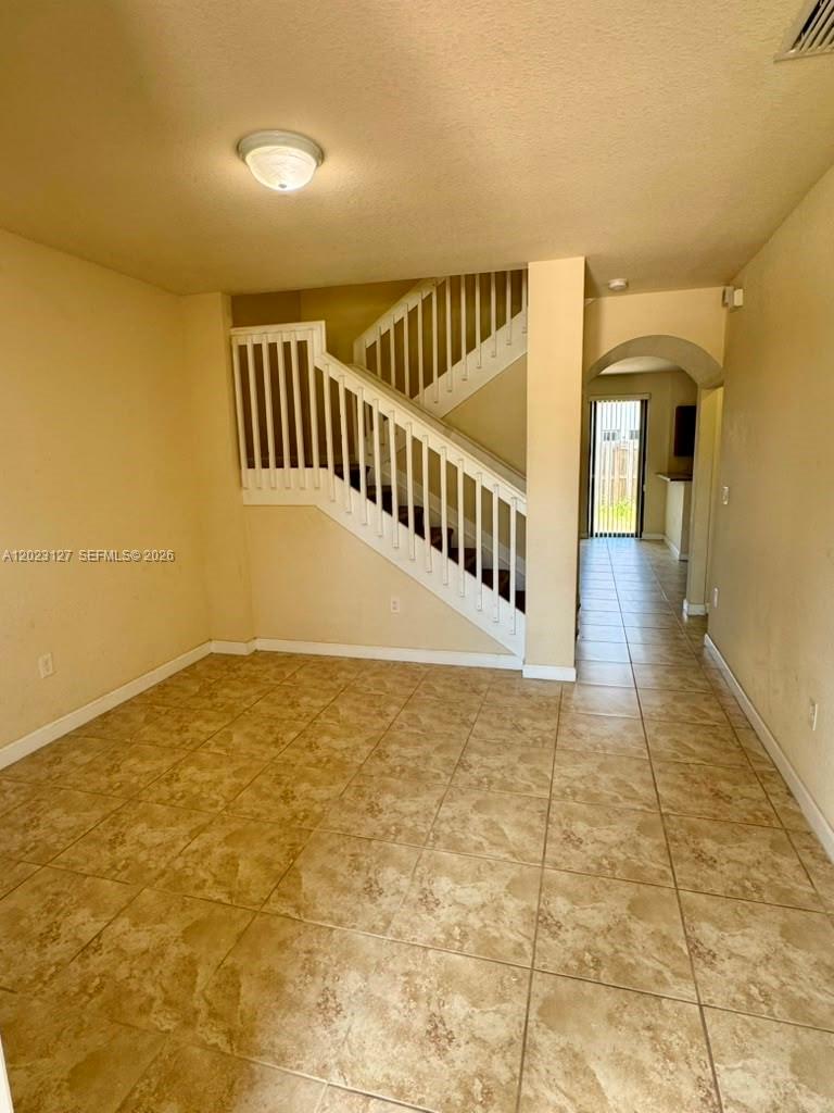 This room features light-colored tile flooring and a white wooden staircase with railings — HOMESTEAD, FL