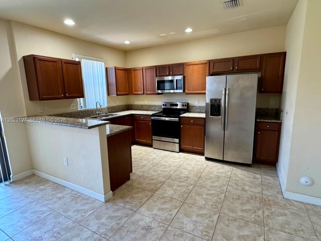 A kitchen features wood cabinets, granite countertops, and stainless steel appliances on tiled floors — HOMESTEAD, FL