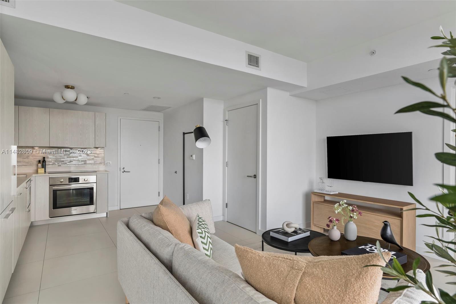 A modern living room and kitchen area features light wood cabinetry, white walls, and tile flooring — 501 NE 31st St # 3409, Miami FL 33137, MIAMI, FL