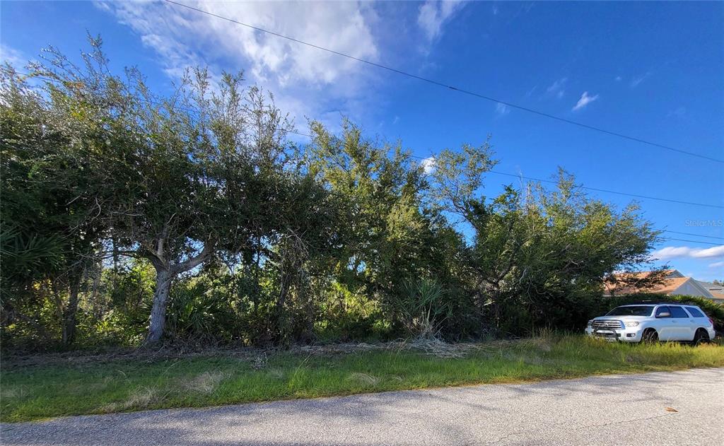 A white SUV is parked on a paved road in front of a wooded lot — 9213 & 9221 GENESEE STREET, PORT CHARLOTTE, FL