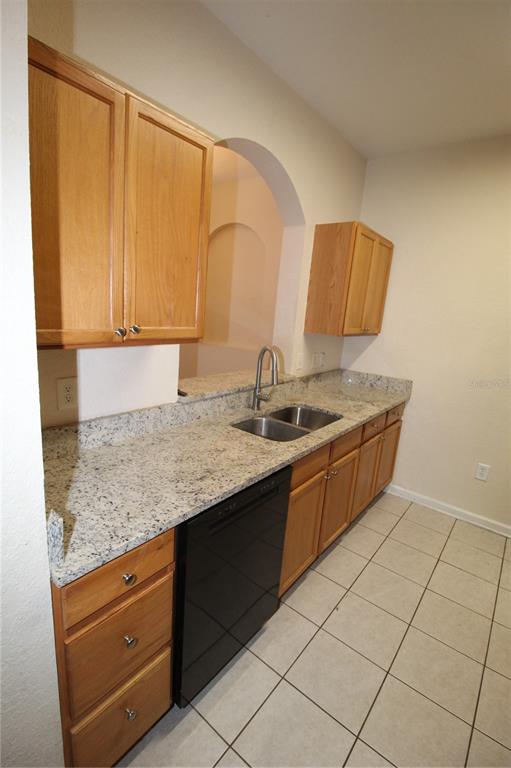 A kitchen features light wood cabinets, granite countertops, a black dishwasher, and tiled flooring — 6380 CONTESSA DRIVE UNIT 208, ORLANDO, FL