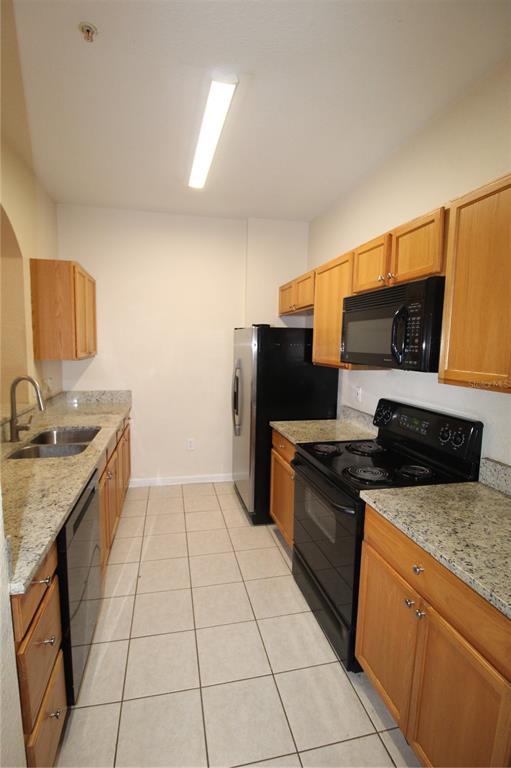 A galley kitchen features light wood cabinets, granite countertops, and black appliances — 6380 CONTESSA DRIVE UNIT 208, ORLANDO, FL