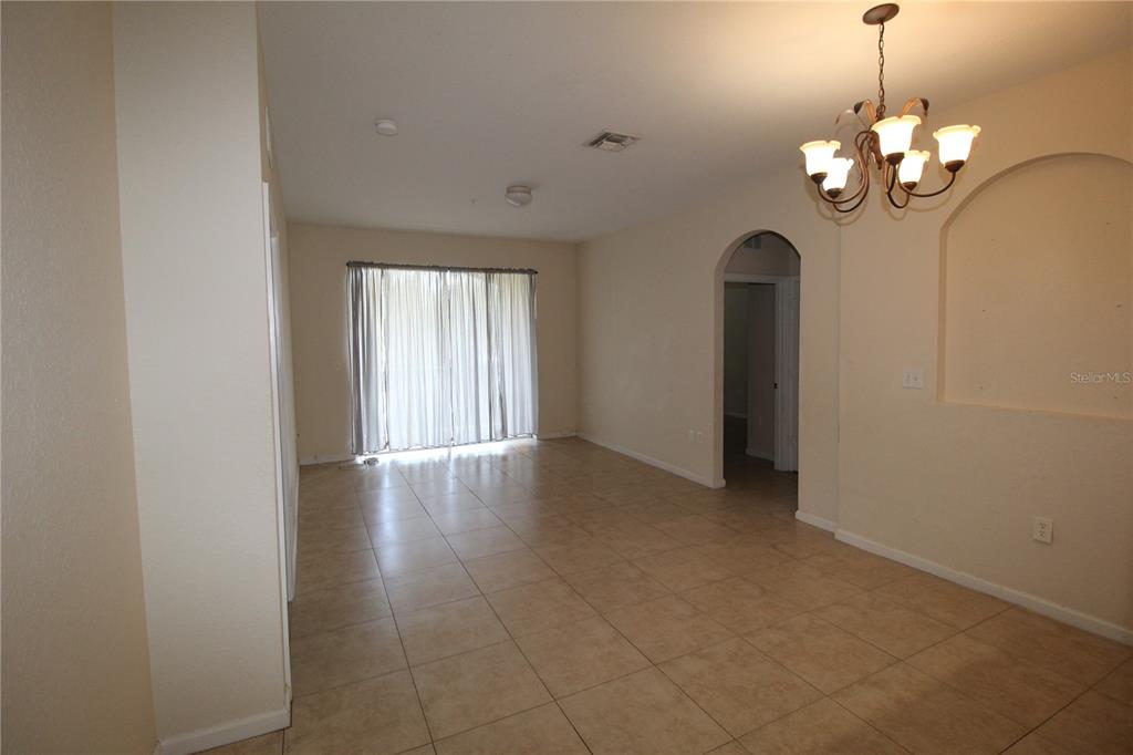 An empty room features beige tile flooring, a chandelier, and sliding glass patio doors — 6380 CONTESSA DRIVE UNIT 208, ORLANDO, FL