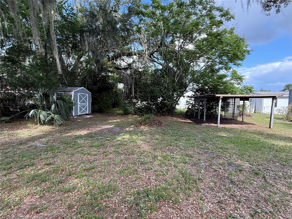 A backyard features a small shed, a covered patio structure, and large oak trees — 806 NEW HAMPSHIRE AVENUE, WILDWOOD, FL