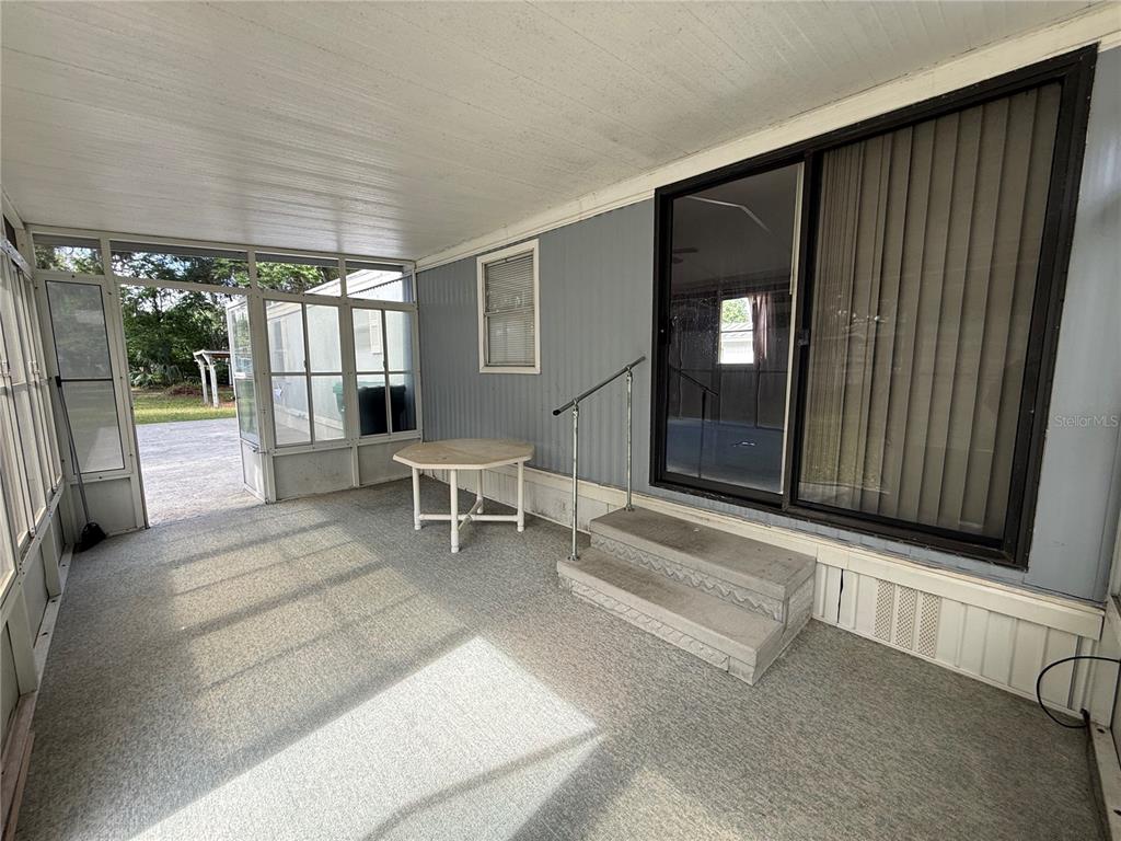 A covered porch features gray carpet, a small round table, and concrete steps leading inside — 806 NEW HAMPSHIRE AVENUE, WILDWOOD, FL
