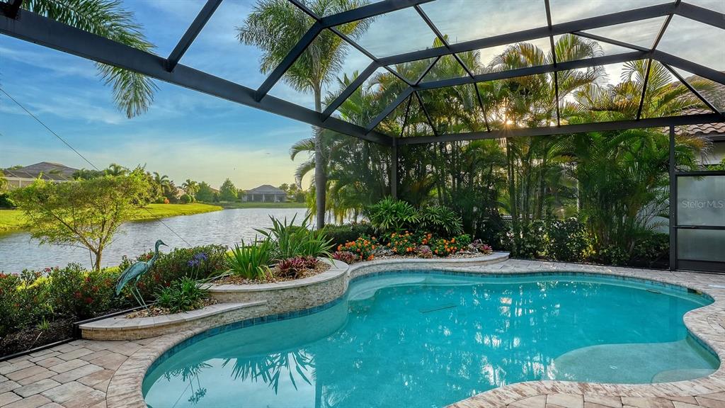 A screened-in pool patio overlooks a lake with lush landscaping and palm trees — 16524 KENDLESHIRE TERRACE, LAKEWOOD RANCH, FL
