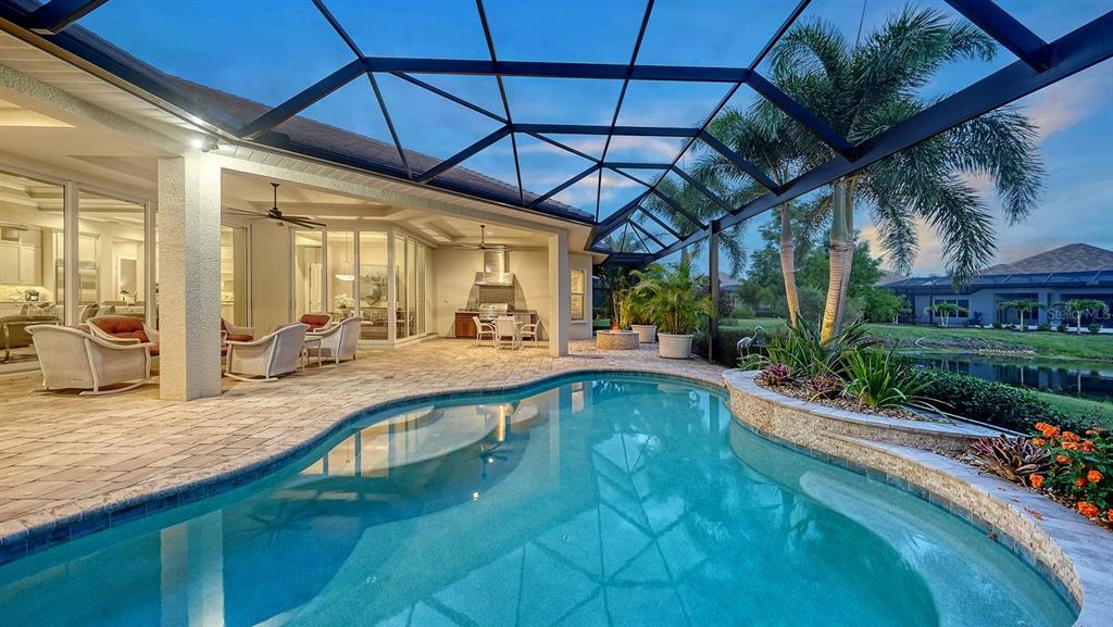 A screened-in patio features a swimming pool, outdoor kitchen, and views of a pond — 16524 KENDLESHIRE TERRACE, LAKEWOOD RANCH, FL