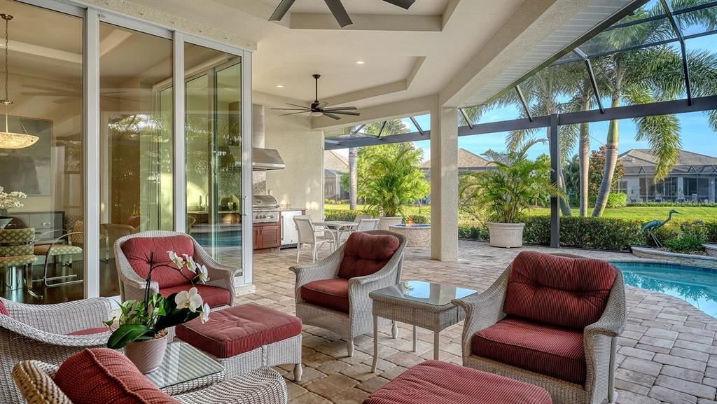 A covered outdoor patio features wicker furniture, a built-in grill, and a swimming pool — 16524 KENDLESHIRE TERRACE, LAKEWOOD RANCH, FL