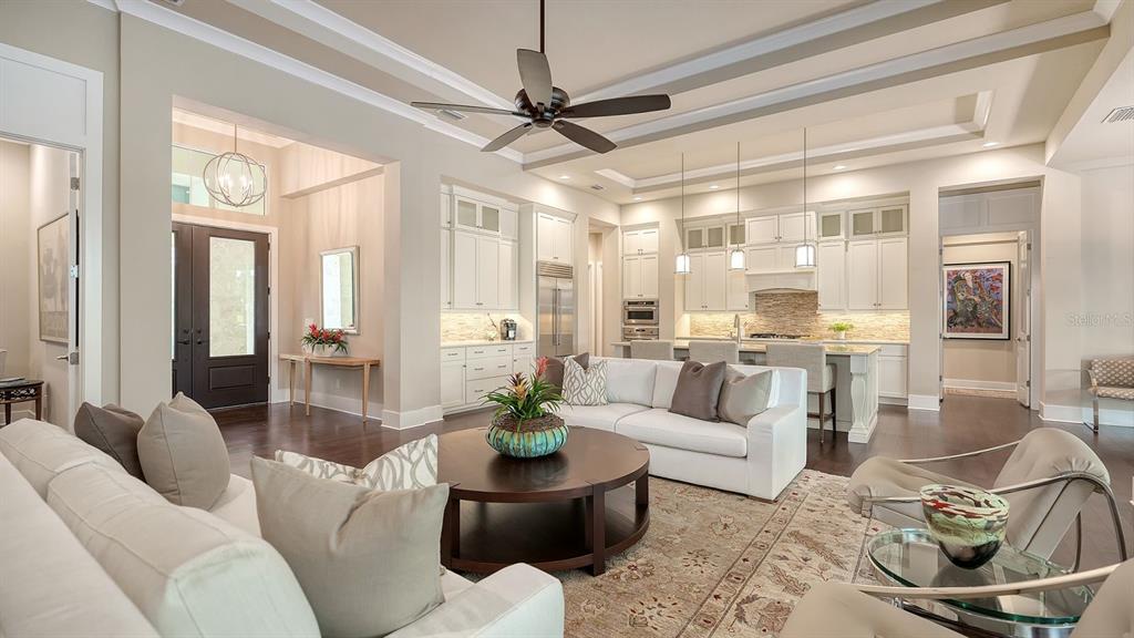 An open-concept living room and kitchen featuring white cabinetry, a large island, and hardwood floors — 16524 KENDLESHIRE TERRACE, LAKEWOOD RANCH, FL
