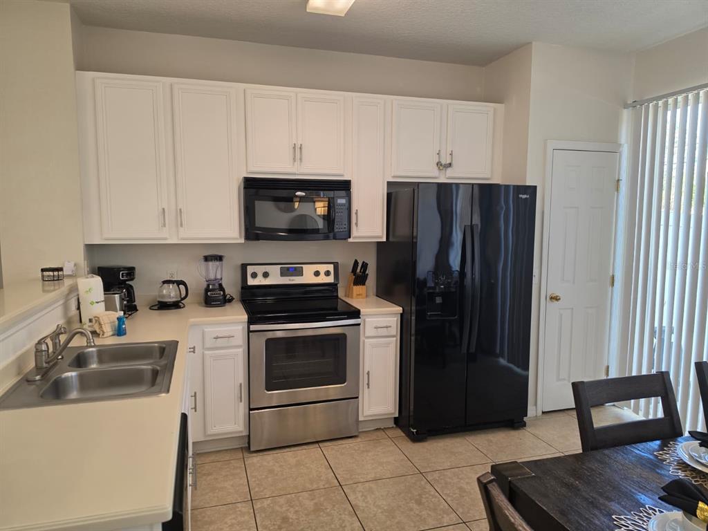 A kitchen with white cabinets, stainless steel appliances, a black refrigerator, and tile flooring — 5520 PARADISE CAY CIRCLE, KISSIMMEE, FL