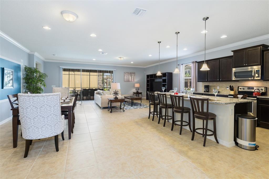 An open-concept kitchen and living area features dark wood cabinets, granite countertops, and tile flooring — 8801 RHODES STREET, KISSIMMEE, FL