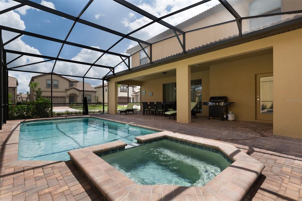 A screened-in patio features a swimming pool, a hot tub, and a gas grill — 8801 RHODES STREET, KISSIMMEE, FL