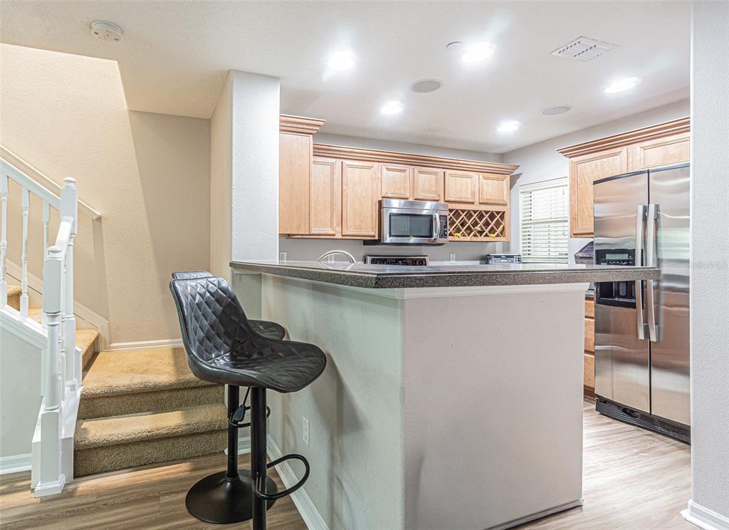 A kitchen features light wood cabinets, stainless steel appliances, a breakfast bar, and adjacent stairs — 526 WHEATON TRENT PLACE, TAMPA, FL
