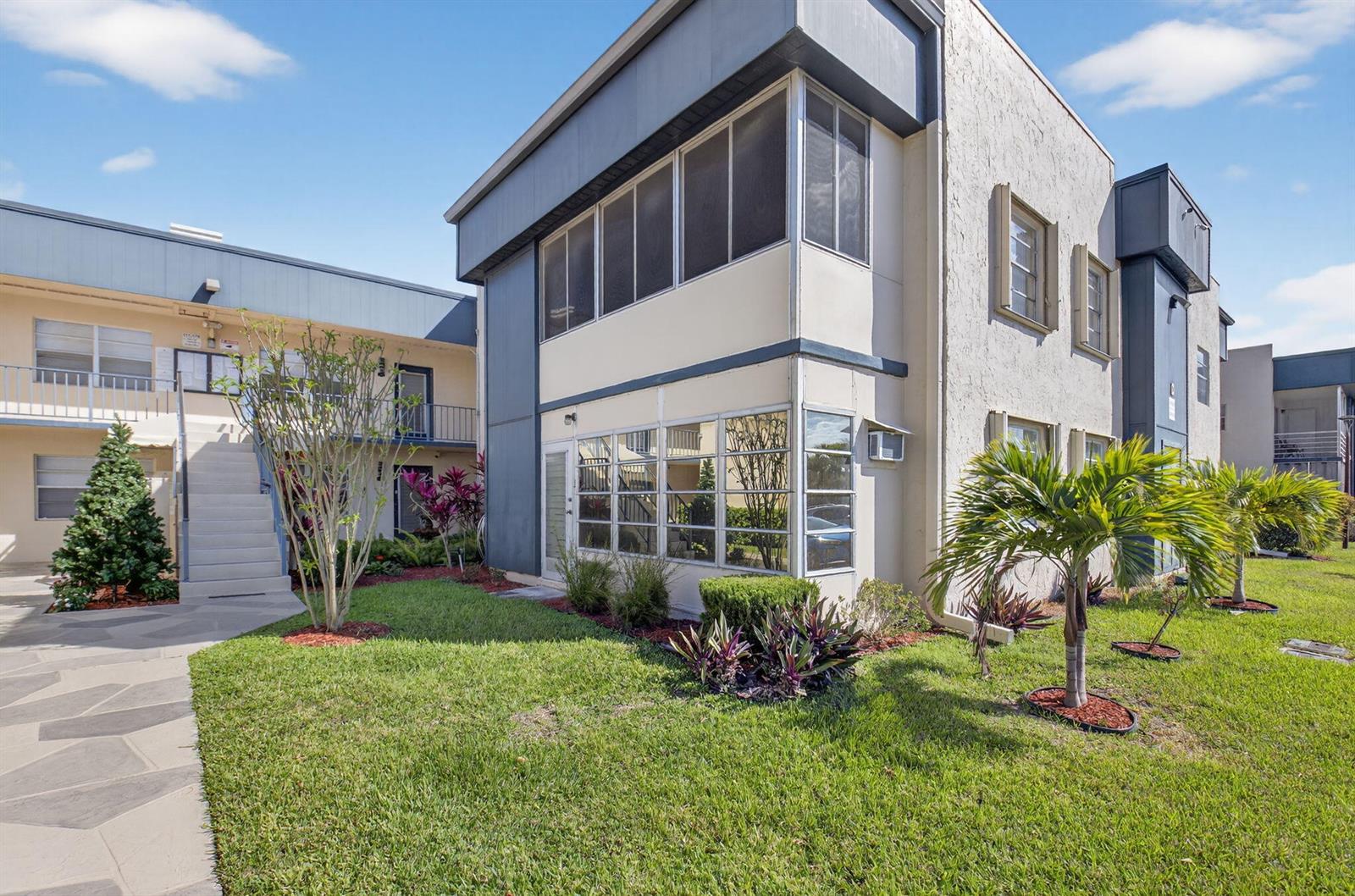 A two-story apartment building exterior with a screened balcony, large windows, and landscaped lawn — 173 Flanders D, Delray Beach FL 33484, DELRAY BEACH, FL