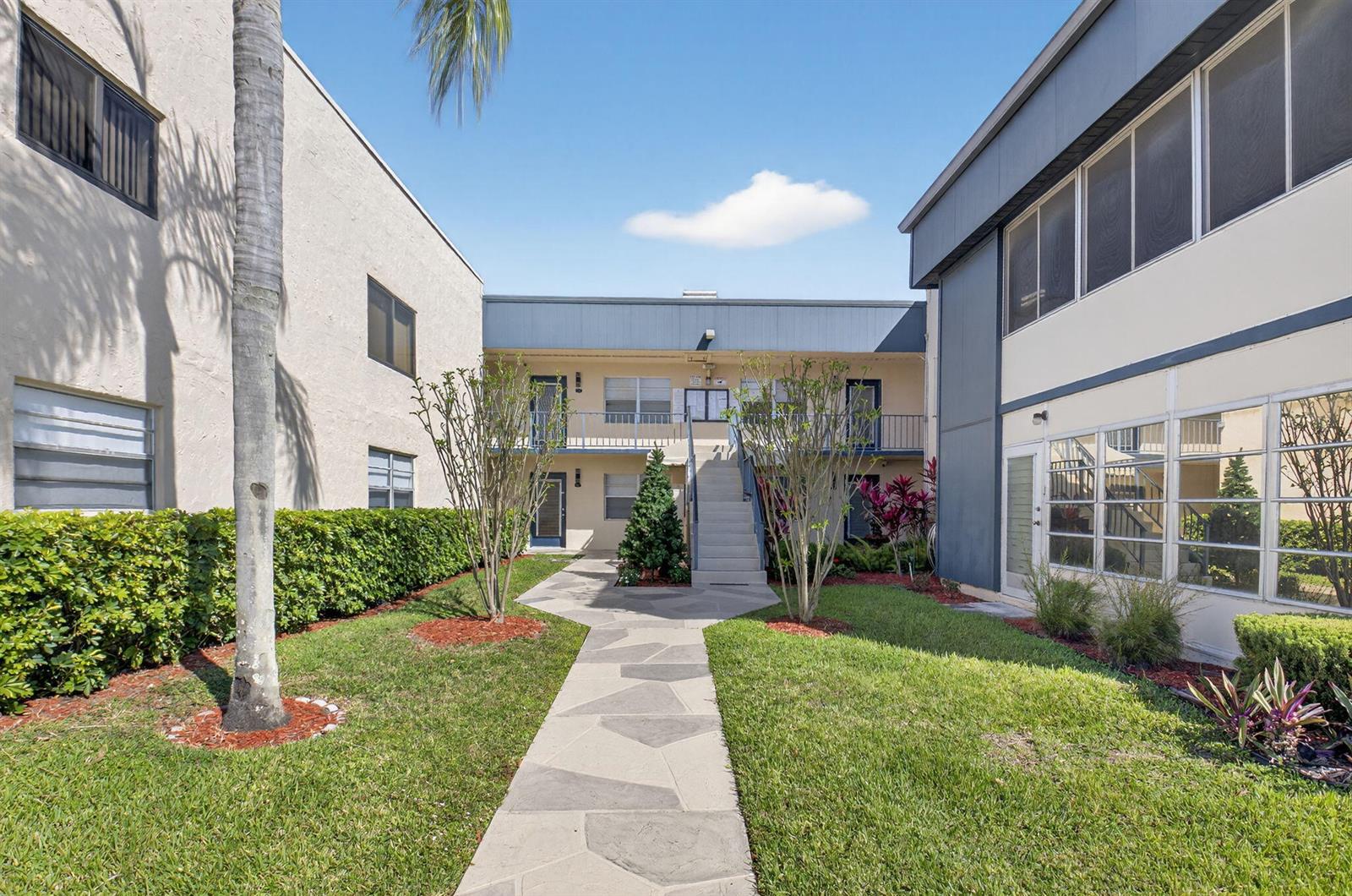 A stone walkway leads to a two-story apartment building with a central staircase and landscaping — 173 Flanders D, Delray Beach FL 33484, DELRAY BEACH, FL