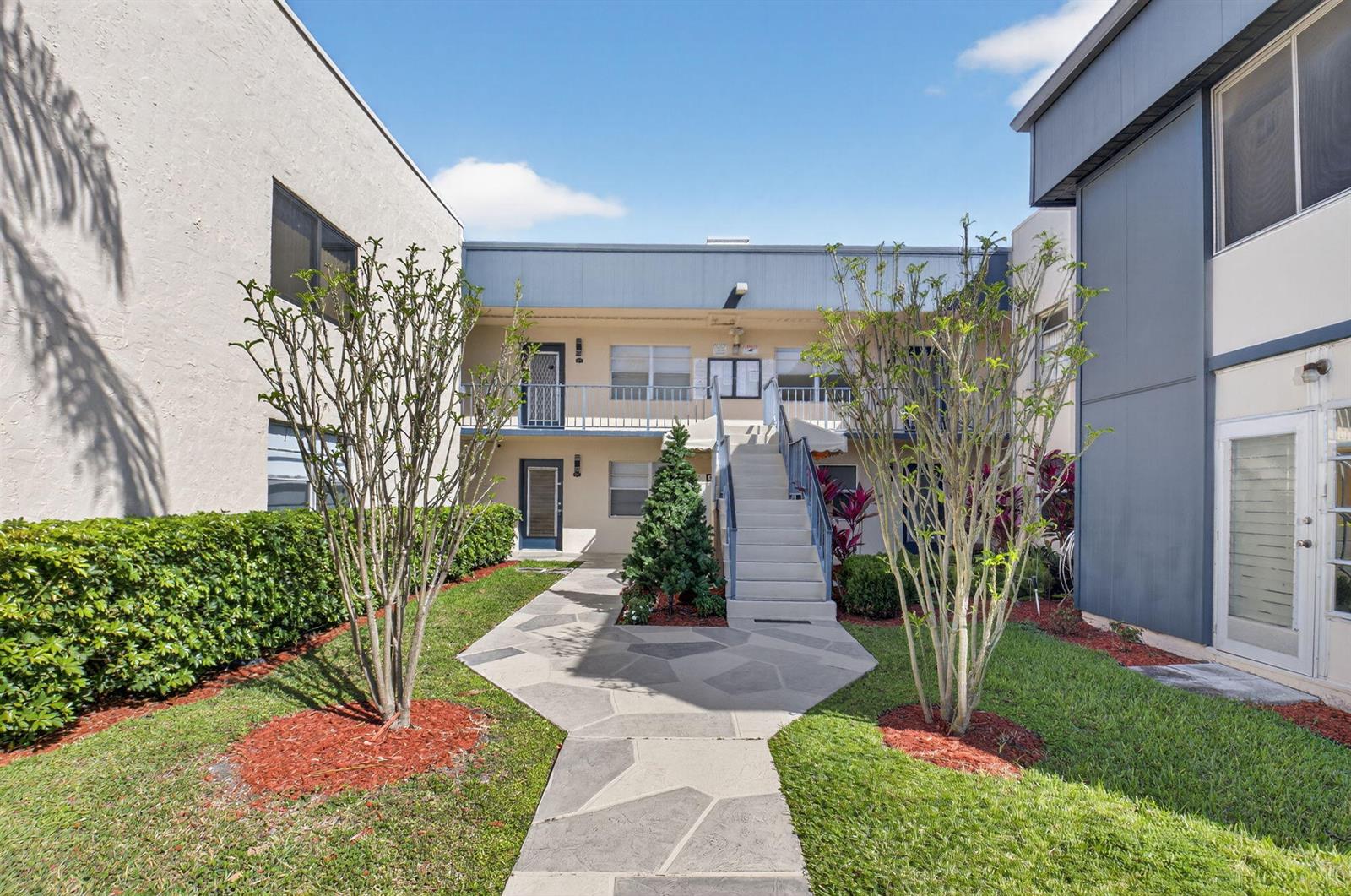 A paved walkway leads to a central staircase between two apartment building wings — 173 Flanders D, Delray Beach FL 33484, DELRAY BEACH, FL
