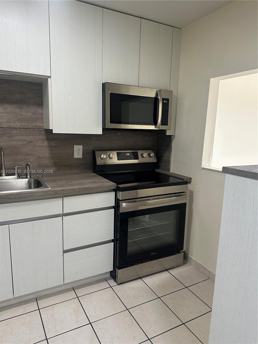 A kitchen features white cabinets, stainless steel appliances, a wood-look countertop, and tiled flooring — 1075 W 68th St # 309, Hialeah FL 33014, HIALEAH, FL