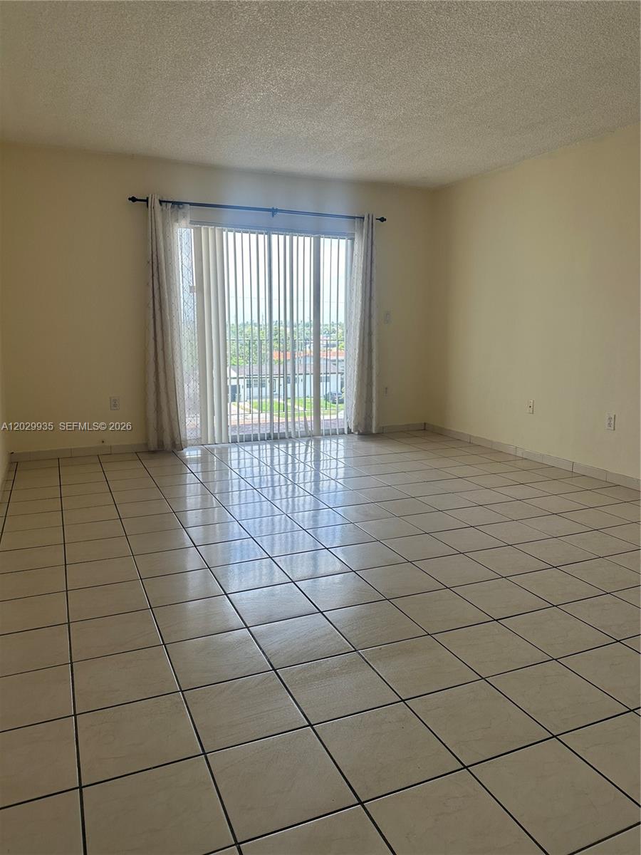 An empty room features light-colored tile flooring, beige walls, and a sliding glass balcony door — 1075 W 68th St # 309, Hialeah FL 33014, HIALEAH, FL