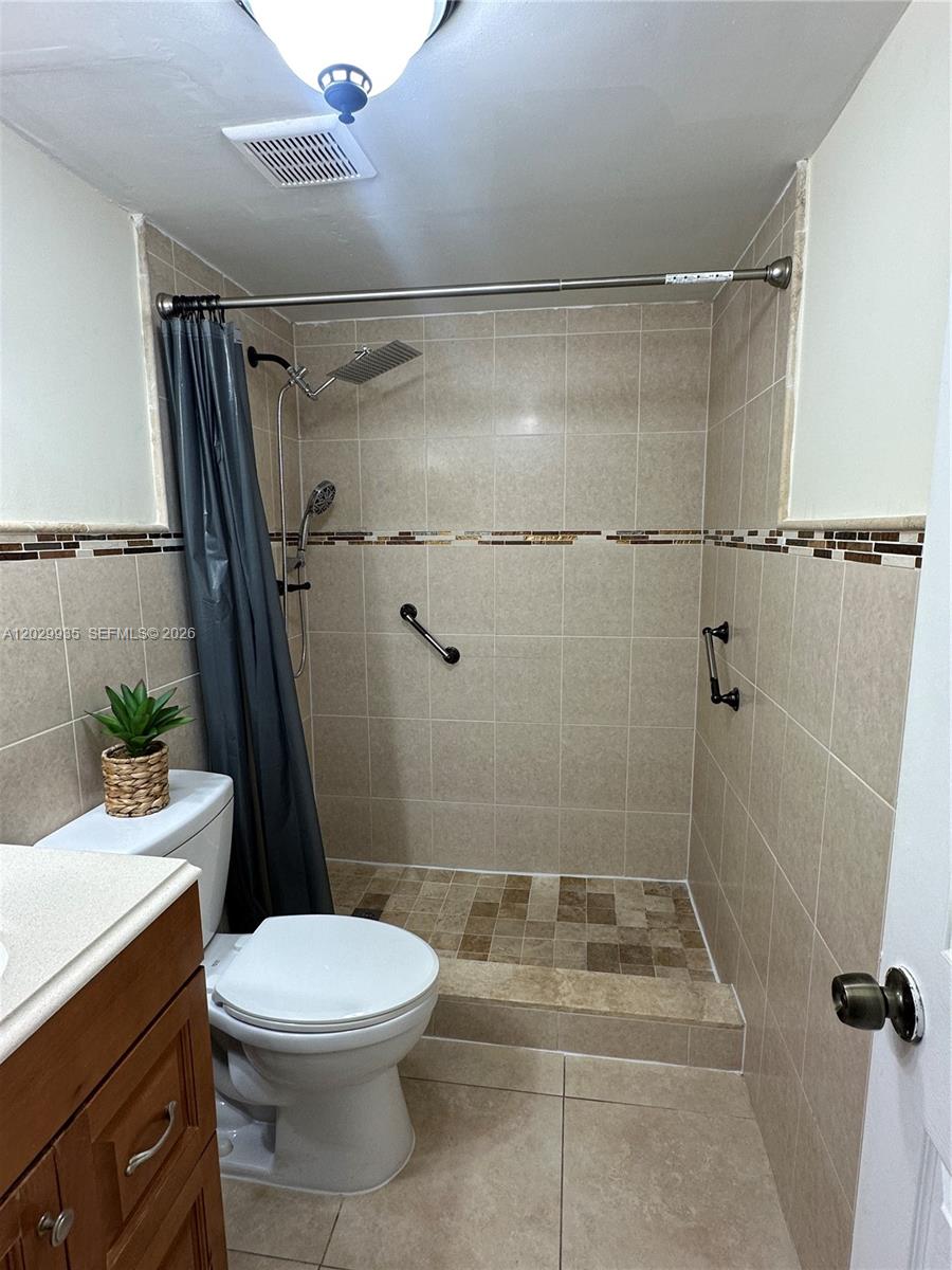 A bathroom features a tiled walk-in shower with grab bars and a toilet nearby — 1075 W 68th St # 309, Hialeah FL 33014, HIALEAH, FL