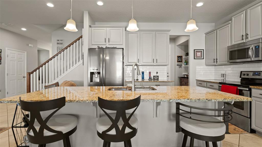 A kitchen features a granite-topped island with three bar stools and light gray cabinetry — 2544 FOLIO WAY, KISSIMMEE, FL