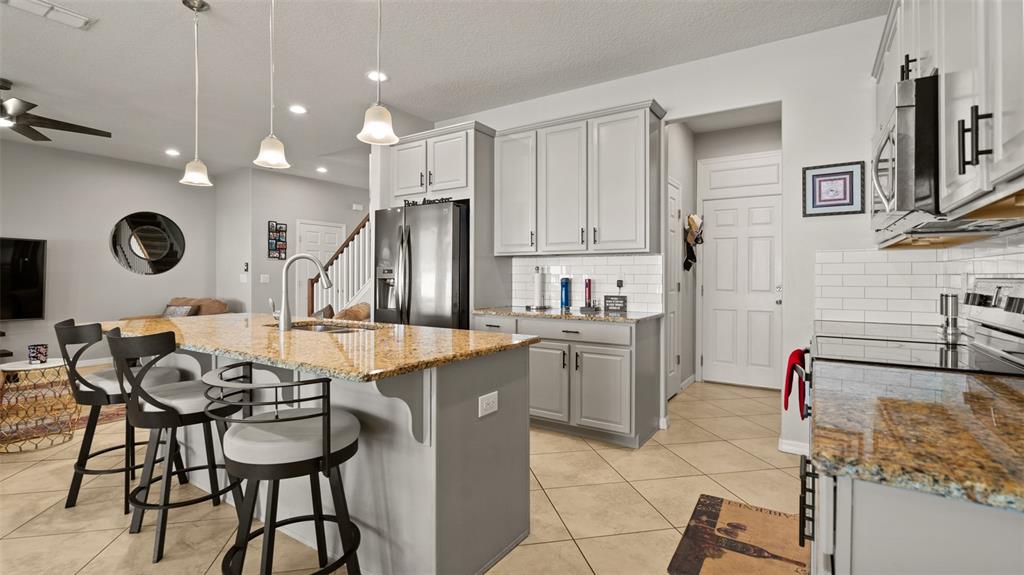 A kitchen features a granite-topped island, gray cabinetry, and tile flooring in an open layout — 2544 FOLIO WAY, KISSIMMEE, FL