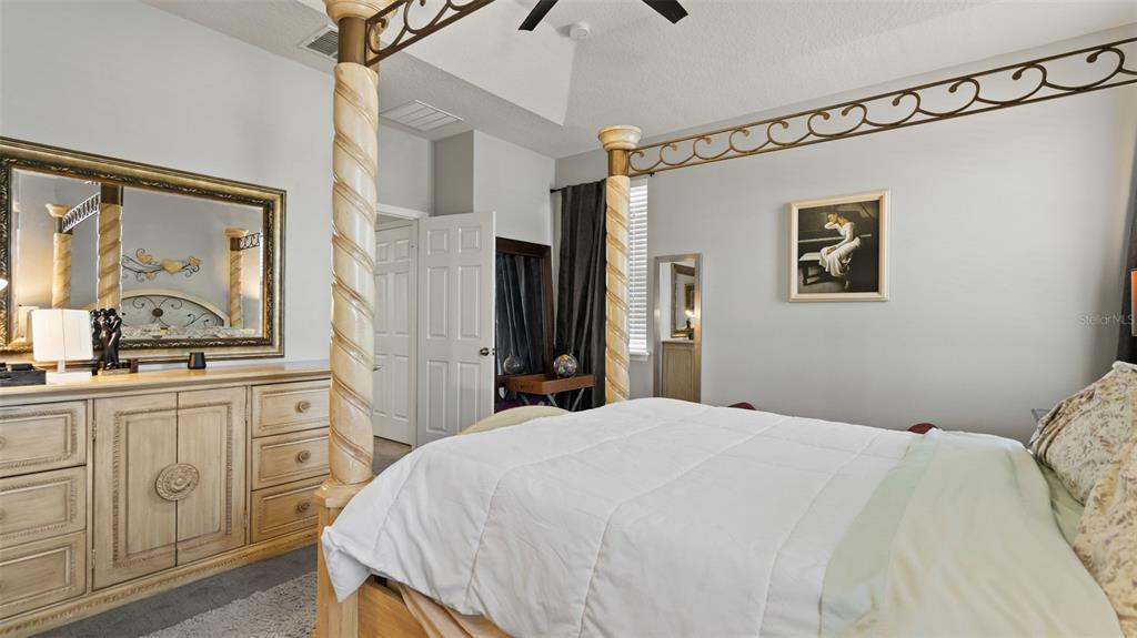 A bedroom features a four-poster bed, a wooden dresser with a mirror, and light walls — 2544 FOLIO WAY, KISSIMMEE, FL